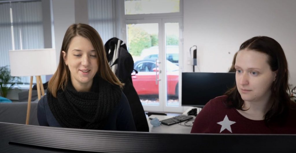 Mitarbeiter von Webseitenschmied sitzen vor Computer, tauschen sich aus